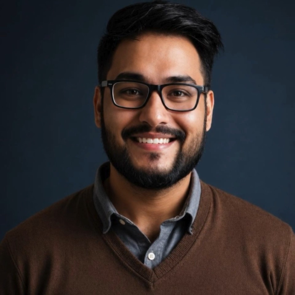 Abhishek Uniyal, bearded and in glasses, in a brown sweater over a grey collar against a dark blue ground